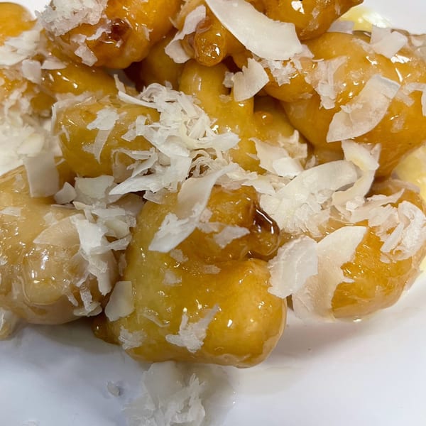 Close-up of golden fried banana fritters, glazed with honey and sprinkled with coconut flakes.